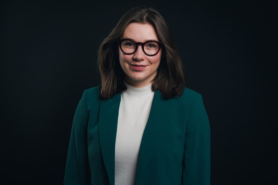Business-Portrait einer jungen Frau mit Brille und grünem Blazer vor dunklem Hintergrund
