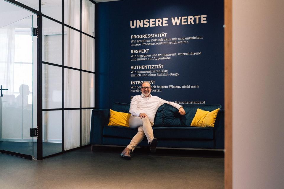 Berater sitzt auf dem Sofa vor der Wand mit den Unternehmenswerten von grynia consulting