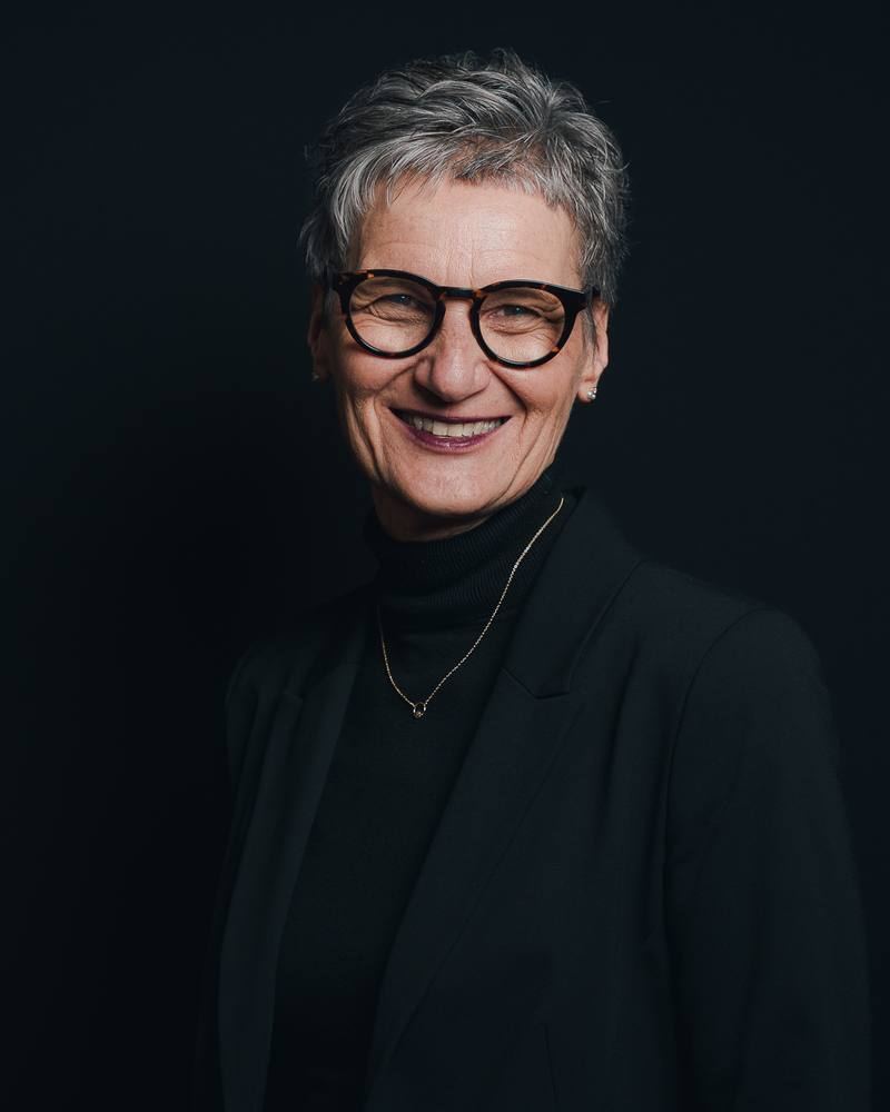 Business-Portrait einer Frau mit Brille vor dunklem Hintergrund